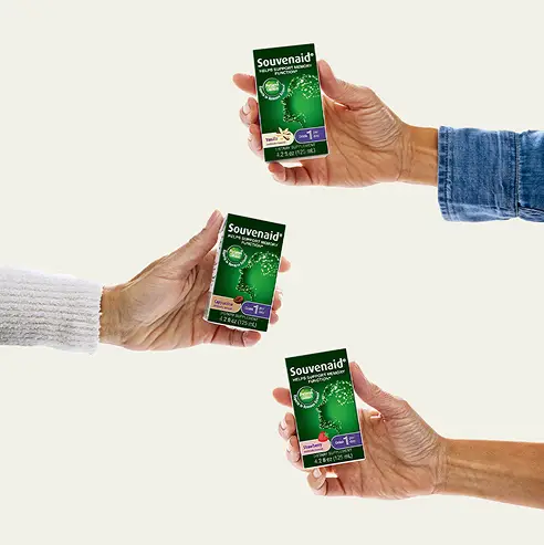 Three hands, each holding a green box of Souvenaid nutritional supplement, are shown against a plain light background—a dynamic visual for consumer health marketing and effective product launch campaigns. The boxes feature a brain graphic and “Cappuccino” or “Vanilla.”.