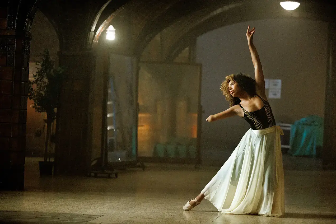 A ballet dancer in a white skirt and black top poses gracefully on pointe under an arched, dimly lit hallway, her form reflecting the poise and strategy needed for a successful product launch or effective brand strategy.