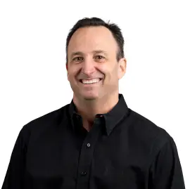 Smiling man with short dark hair wearing a black button-up shirt, standing against a plain white background—reflecting the professionalism and agency core values of a leading healthcare marketing agency.