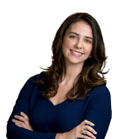 A woman with long brown hair wearing a navy blue top smiles confidently with her arms crossed, embodying the agency core values of a leading healthcare marketing agency against a plain background.