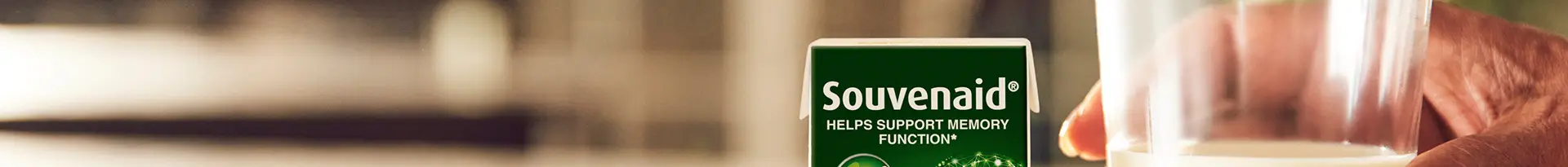 A hand holds a glass of a light-colored drink next to a green box labeled Souvenaid HELPS SUPPORT MEMORY FUNCTION, highlighting our work in MedTech marketing agency healthcare product launch strategy. The background is blurred.
