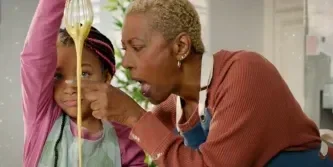 Adult helping a child stretch melted cheese while cooking together in a kitchen.