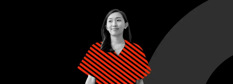 A woman stands confidently against a black background with modern geometric shapes, including a solid red square and a large dark gray arc—evoking the bold creativity of healthcare marketing and brand strategy. Red diagonal stripes overlay her clothing, adding a graphic design element.